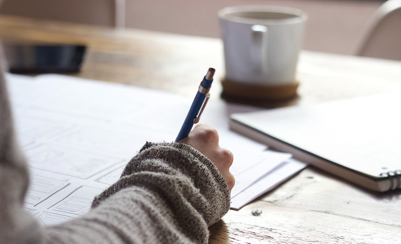 Person with sweater writing with a pen on paper